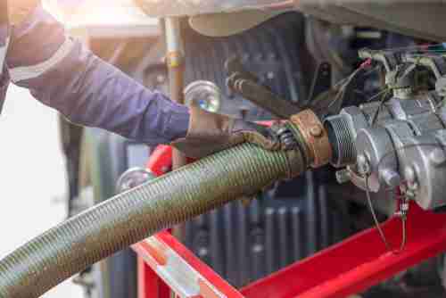 A worker connecting a fuel hose to a tank during a fuel transfer process.